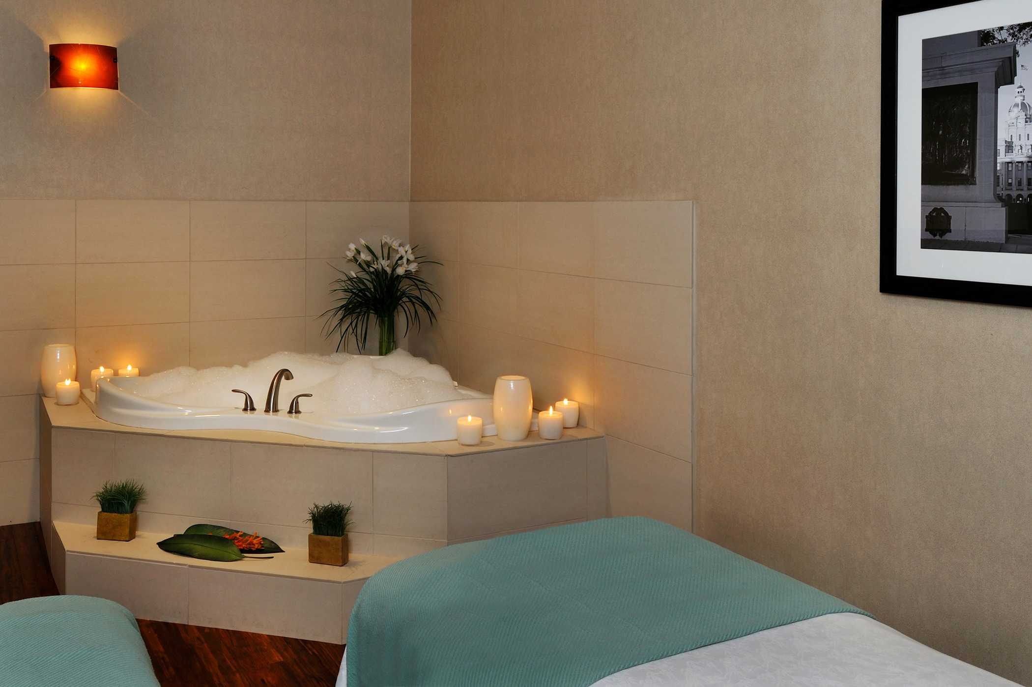 a spa tub prepared with a bubble bath, lit candles and the massage table set